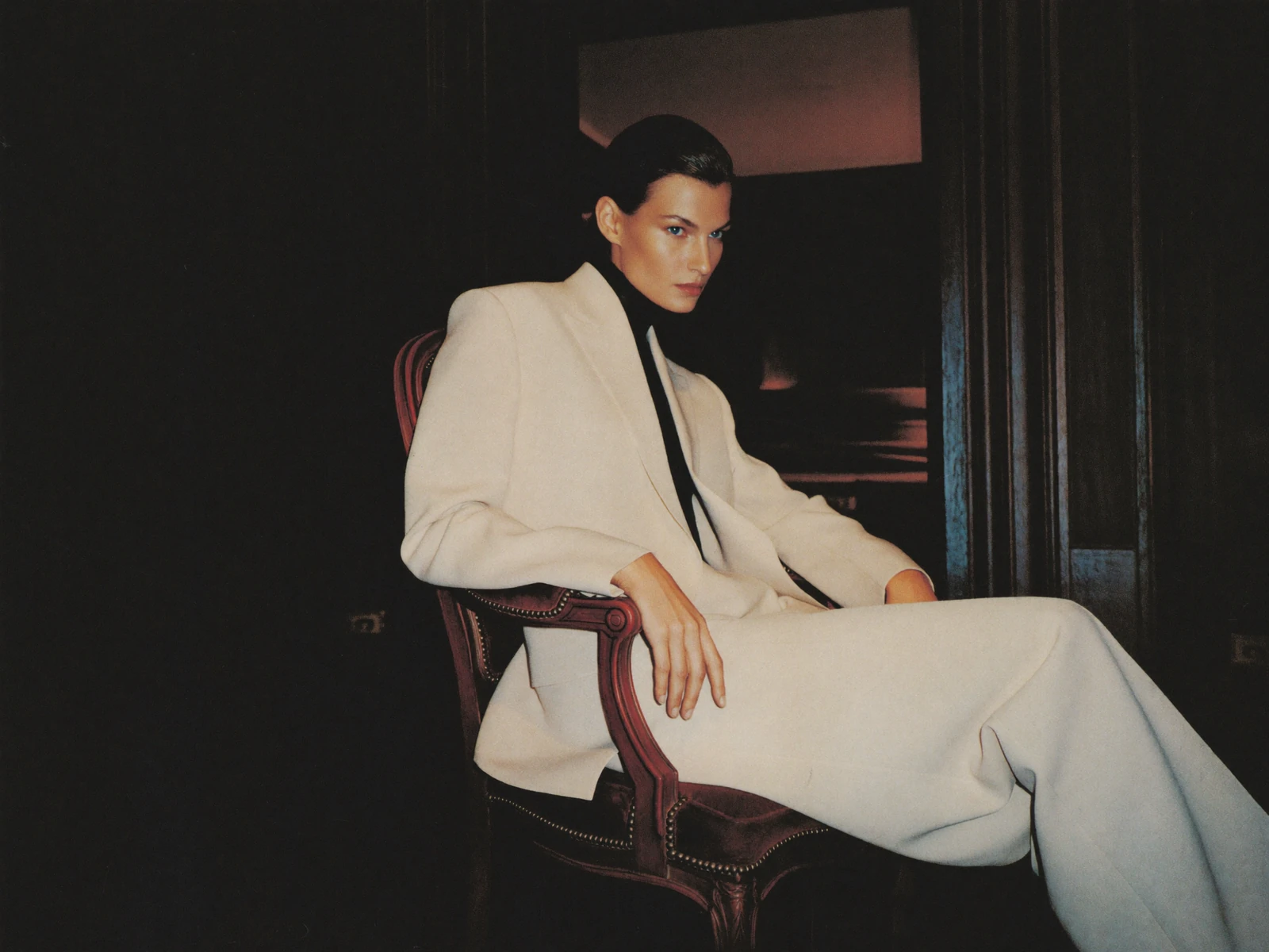 Fashion portrait in an ivory tailored suit, seated in a dark wood room